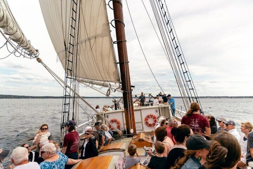 A sailboat with a crowd of people on deck, a lifebuoy, and a calm body of water in the background. 3