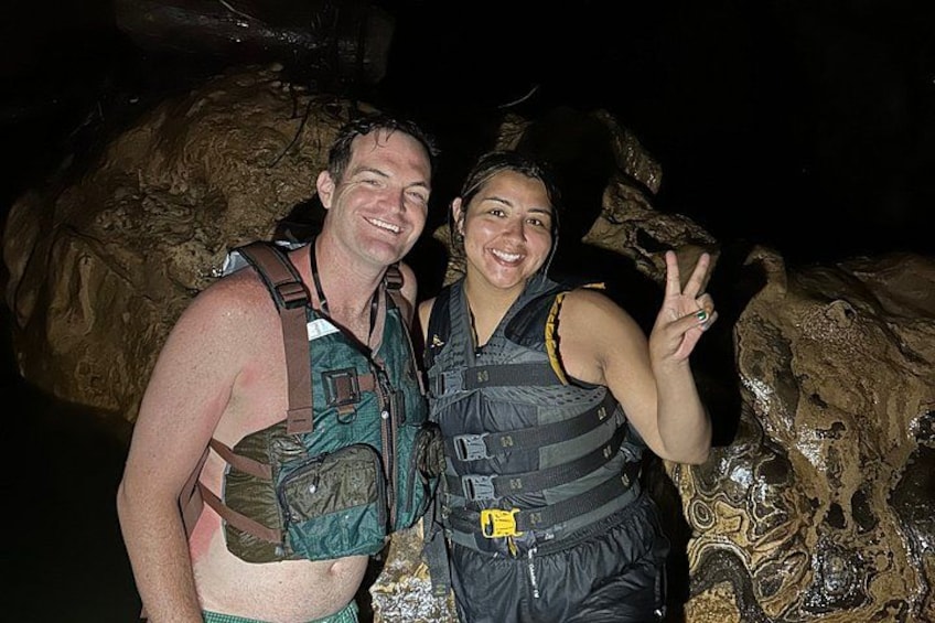 Two people in outdoor gear, one making a peace sign, standing in front of a rocky landscape. 4