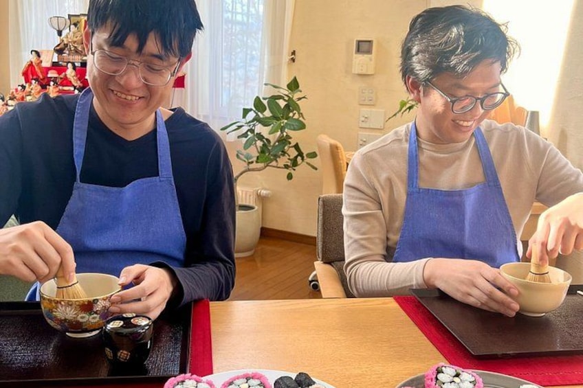 Two people in aprons preparing food at a table with bowls and chopsticks. 2
