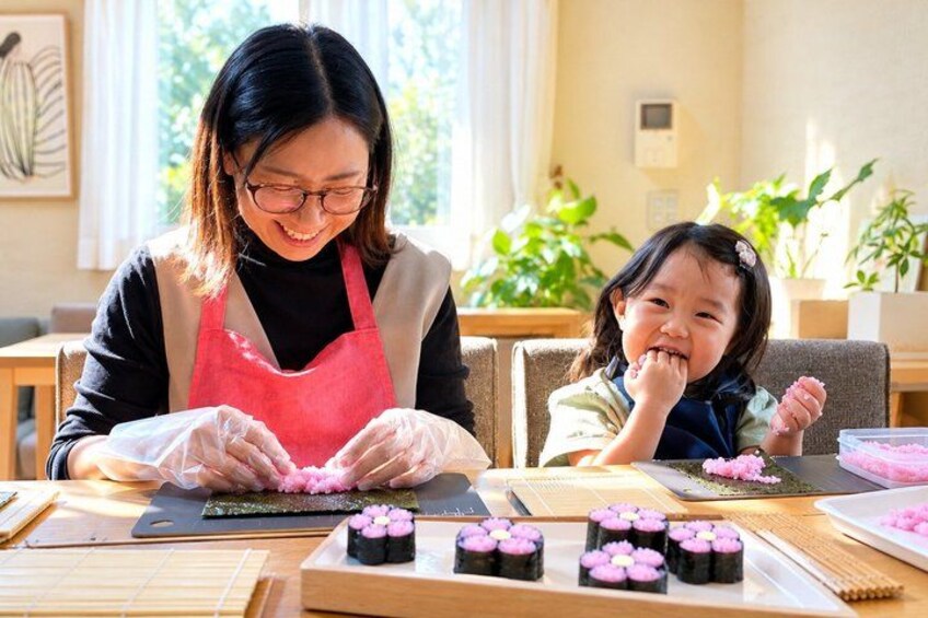 A person preparing food with a child, with a table full of food items and a plant in the background. 4