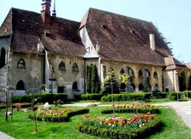 A historic building with a courtyard featuring flower beds and trimmed hedges. 2