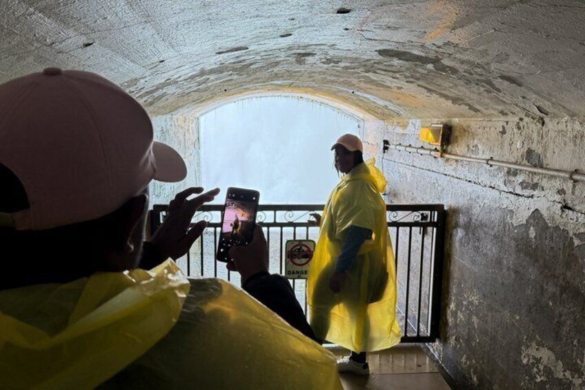 A person in a yellow raincoat and cap taking a photo of another person in a yellow raincoat walking through a tunnel. 4