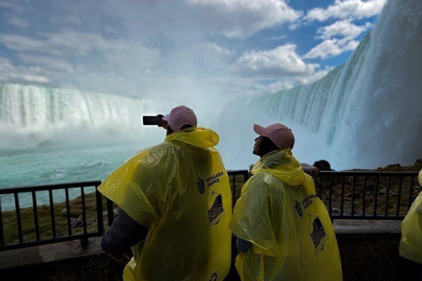 Two people in yellow rain ponchos observing a waterfall. 3