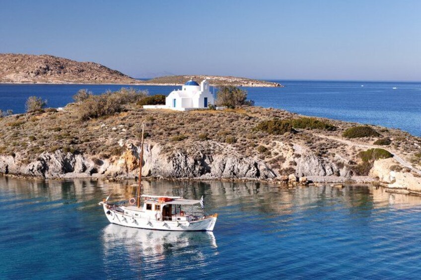 Un barco blanco con cabina roja, un edificio blanco con cúpula azul y una costa rocosa con agua azul cristalina. 1