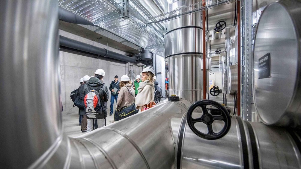 A group of people in a metallic industrial setting with large pipes and control wheels. 2