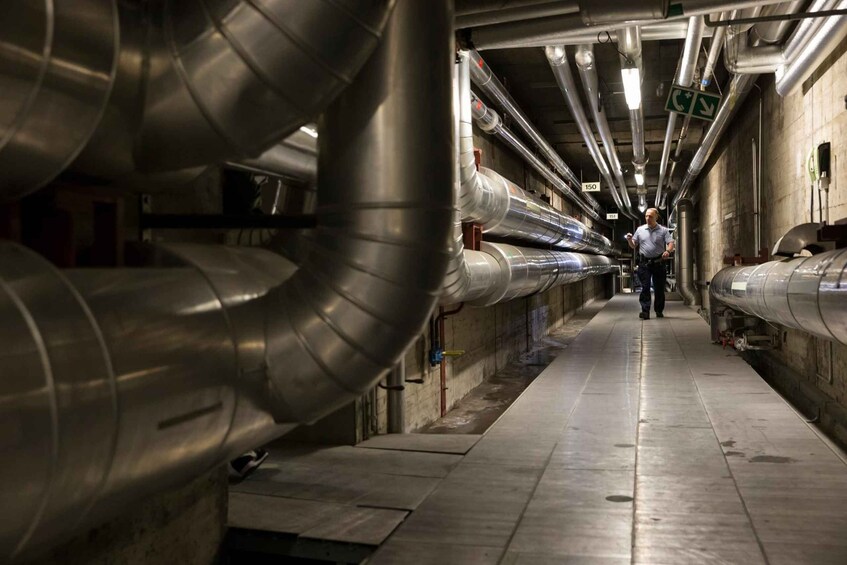 A subway station with metallic ventilation ducts and a person walking down the platform. 3