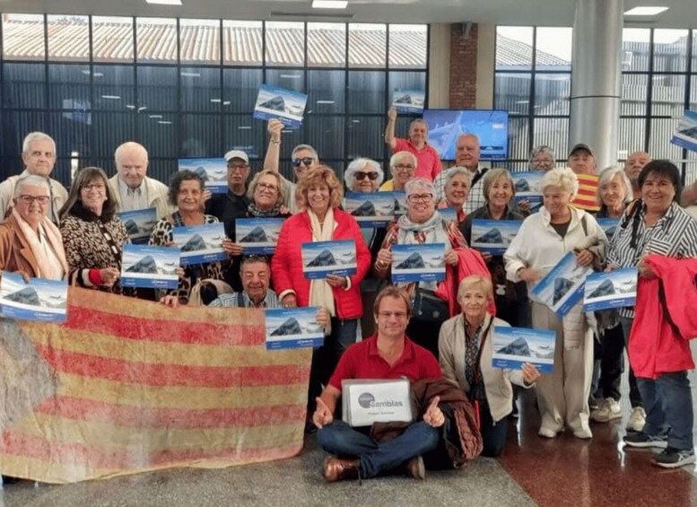 A group of people holding brochures and a large flag, indoors with a modern building and windows in the background. 2