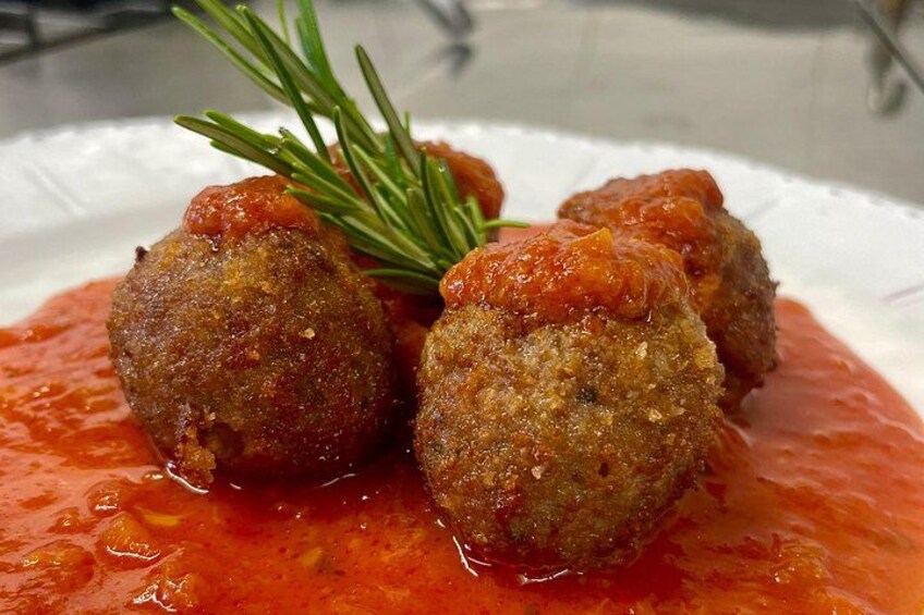 A plate of meatballs with a tomato-based sauce and a sprig of rosemary. 5