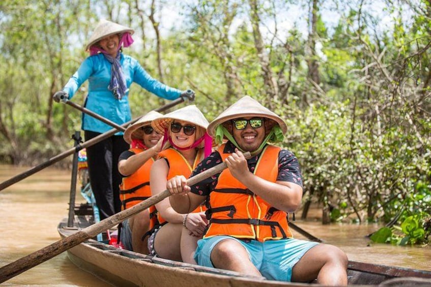 People in a boat wearing life jackets and hats, paddling through a mangrove forest. 1