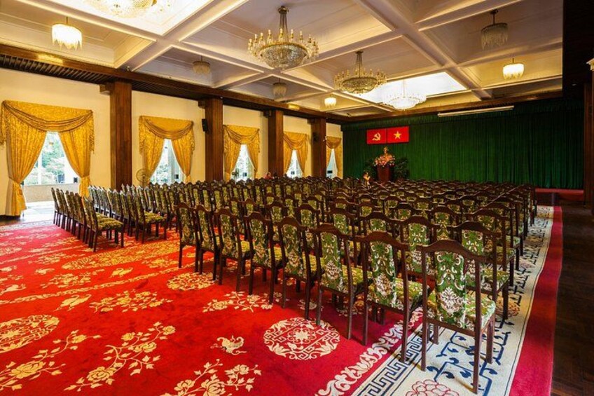 A hall with rows of chairs, a red carpet, chandeliers, and a flag. 2