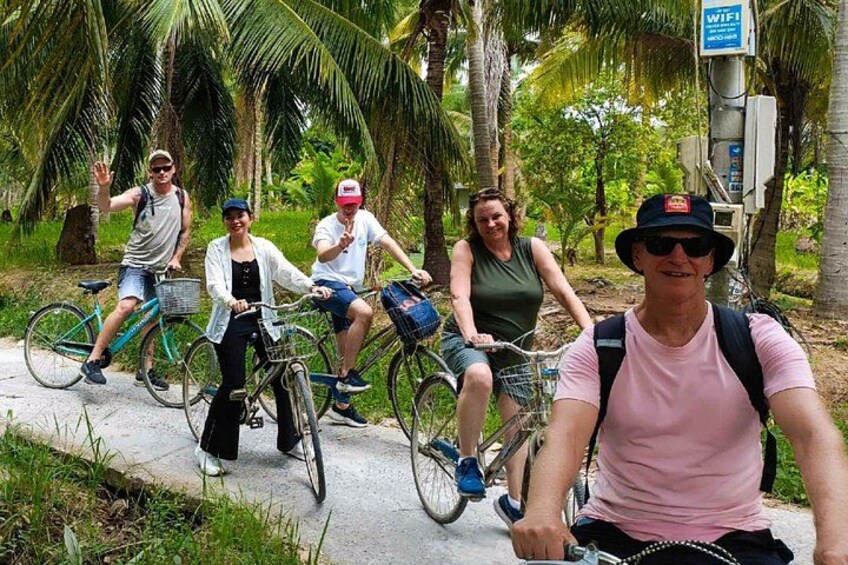 Four people riding bicycles on a path surrounded by palm trees. 4
