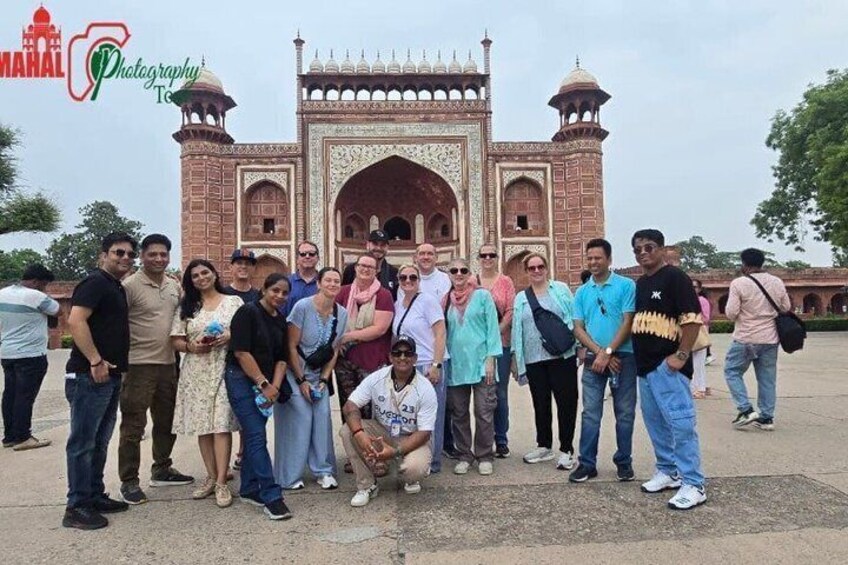 A group of people posing in front of a large, ornate gate with intricate designs and two domed towers. 2