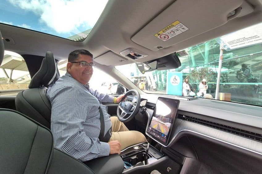 A man driving a car with a sunroof, a digital dashboard, and a rearview mirror. 4