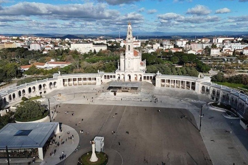 A large open plaza with a central monument, surrounded by buildings and trees. 1
