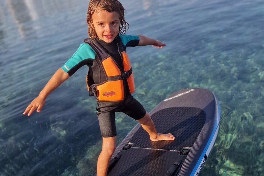 A child on a paddleboard in clear water. 4