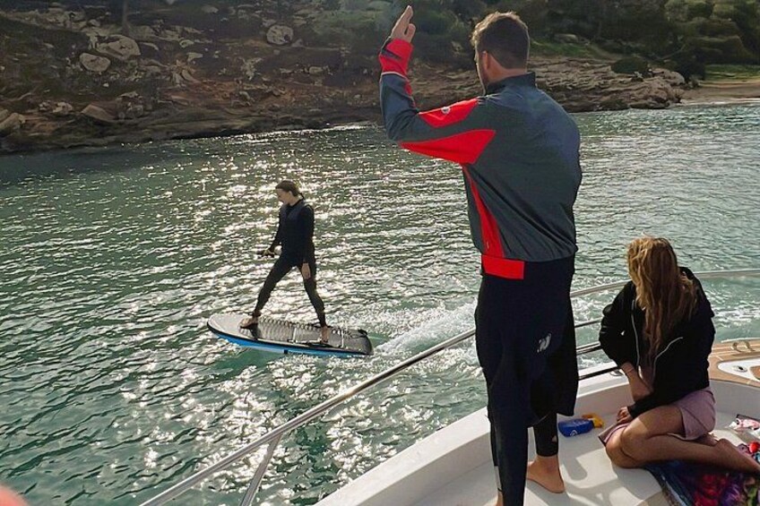 A person paddleboarding on a body of water, a boat with people on board, and a rocky shoreline in the background. 5