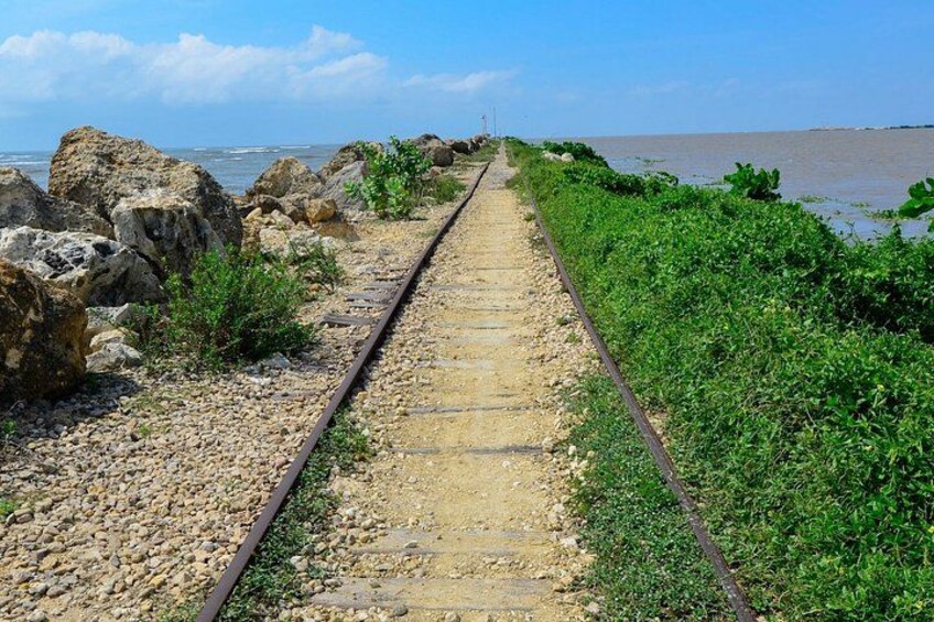 A railway track leading to a body of water, surrounded by rocks and greenery. 5