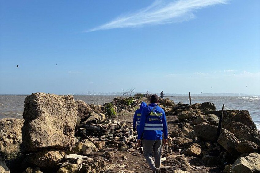 A person walking along a rocky shoreline with large boulders and the ocean in the background. 4