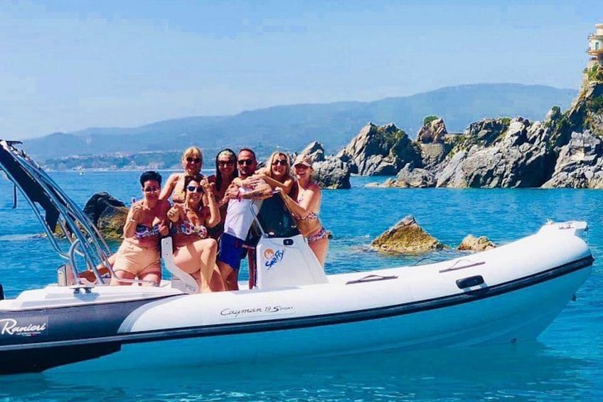 A group of people on a boat with rocky coastline and clear blue water in the background. 1