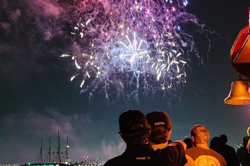 Escena nocturna con fuegos artificiales, gente y una campana grande. 5