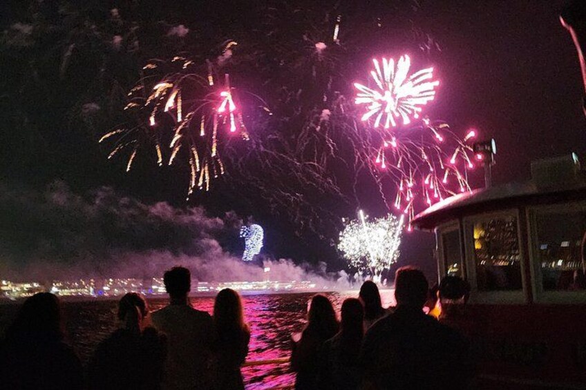 Escena nocturna con fuegos artificiales sobre el agua, siluetas de personas y un barco. 3