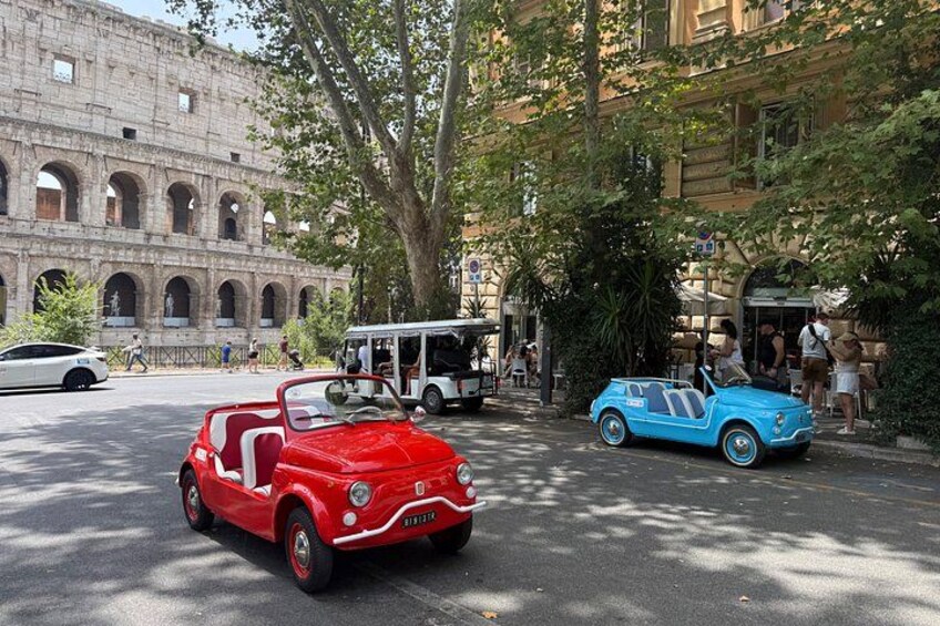A red convertible and a blue car parked on a street with an ancient amphitheater in the background. 5