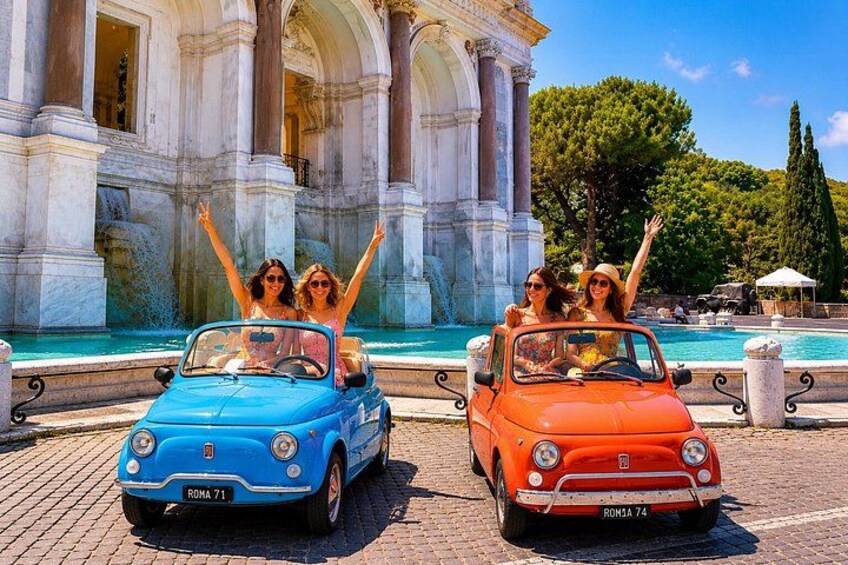 Two vintage cars parked in front of a historic building with columns and a fountain. 2