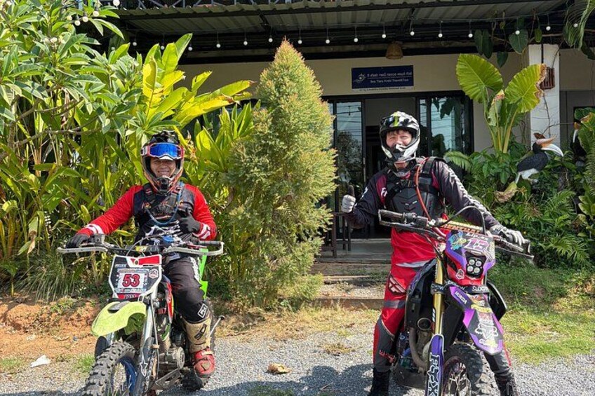 To motorcyklister på offroad-motorcykler foran en bygning med et skilt. 3