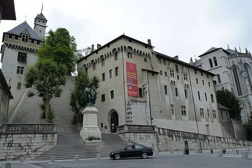 A large historic building with a statue in front, a car parked in front, and a red banner on the building. 3