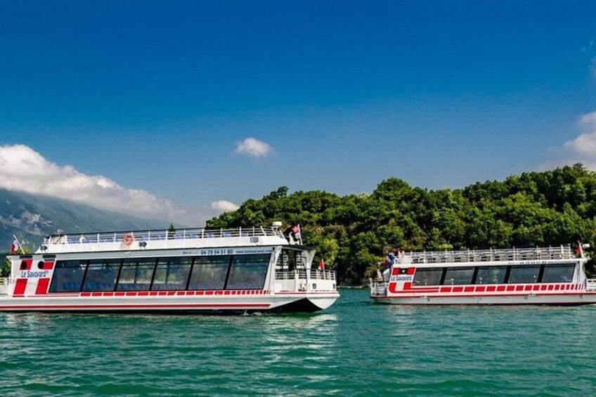 Two large riverboats with red and white stripes, docked on a calm body of water with a forested island in the background. 2