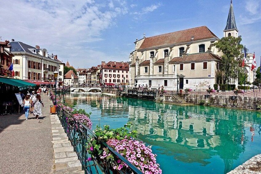 A canal with buildings, a bridge, and flowers along the walkway. 1