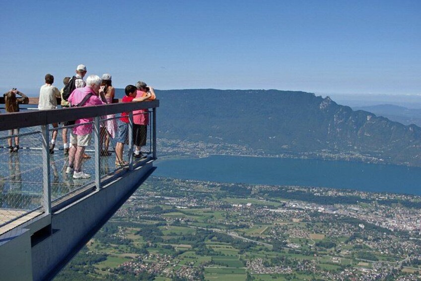People on a glass bridge overlooking a valley with a lake and mountains. 2