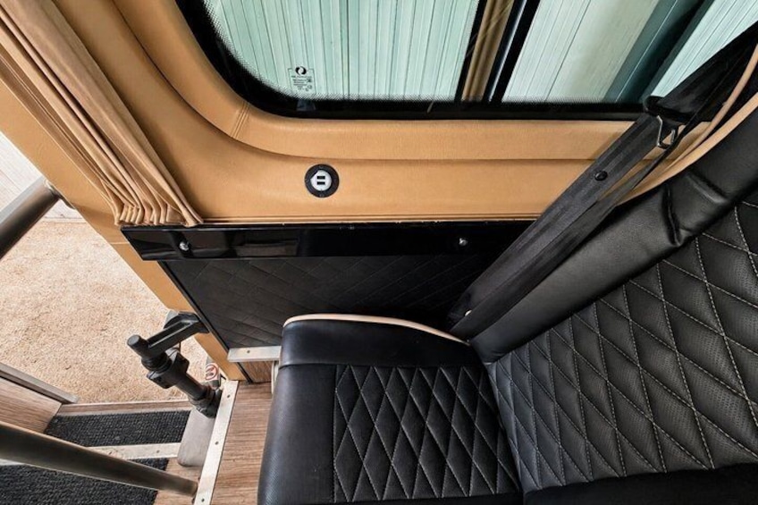 Un habitacle de véhicule avec des sièges noirs à motifs matelassés, un panneau de porte de couleur beige et une vitre teintée en vert. 3