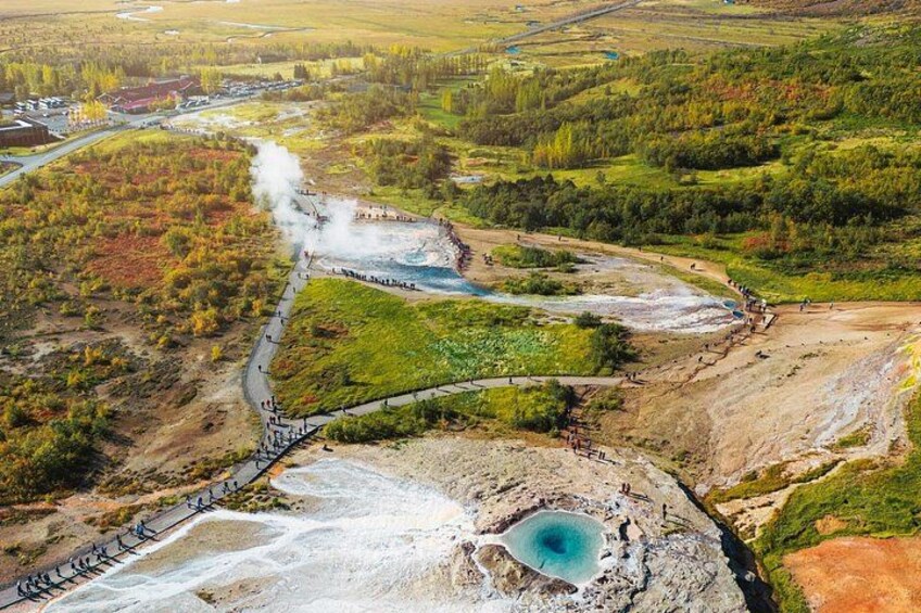 A geothermal area with a steam vent, a turquoise hot spring, and a paved walkway. 4