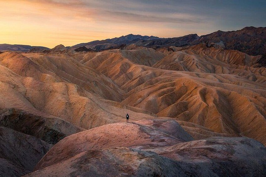 A person standing on a rock in a desert landscape with undulating hills and mountains in the background. 4