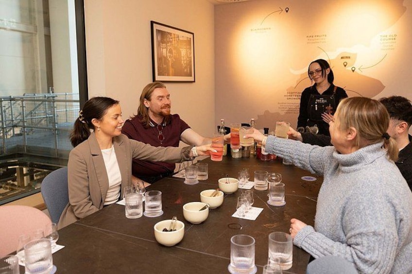 A group of people sitting around a table with various items, including bowls and glasses, in a room with a large window and a wall with text. 1