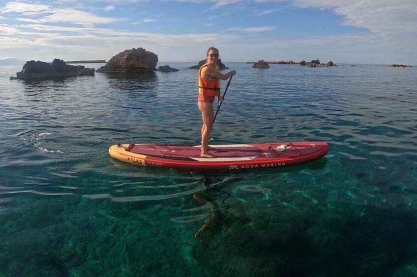 Une personne fait de la planche à pagaie sur une eau claire, avec des rochers en arrière-plan. 2