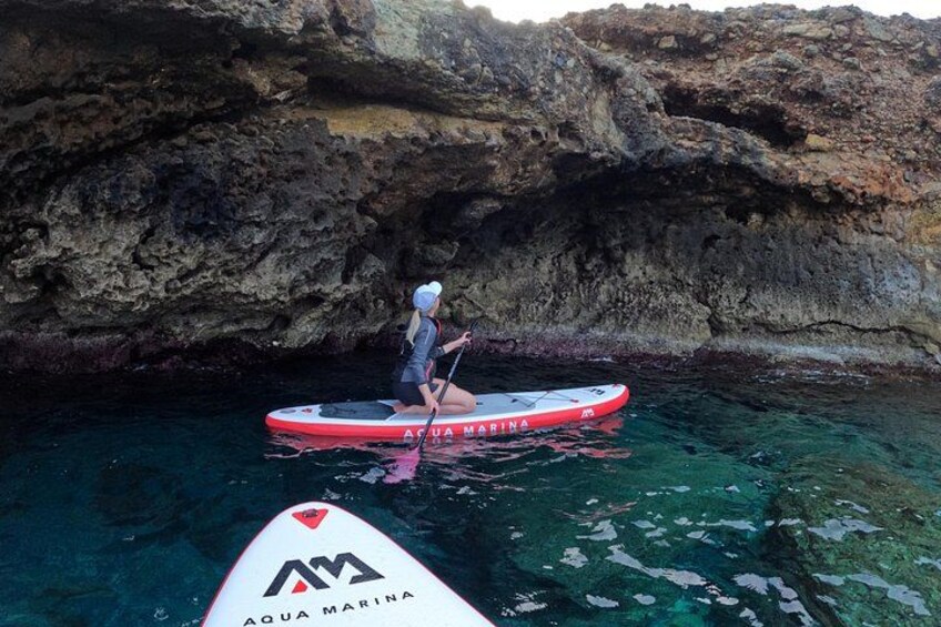Une personne fait de la planche à pagaie sur une planche rouge portant l'inscription « AQUA MARINA », entourée d'une eau cristalline et de falaises rocheuses. 5