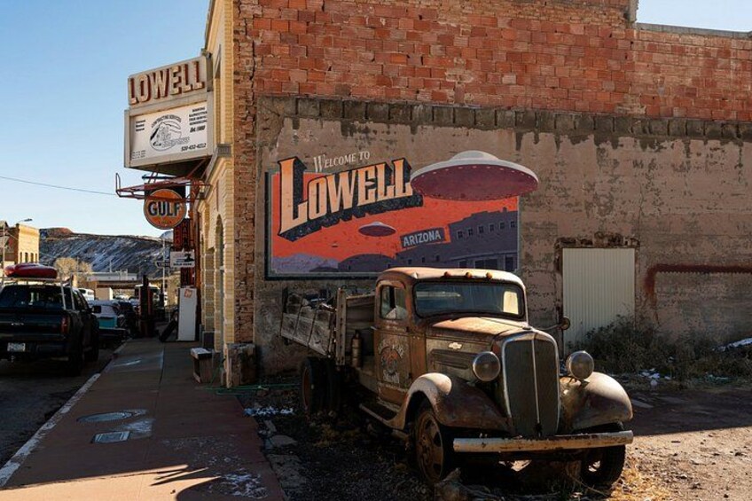 Un camión antiguo estacionado frente a un edificio con un mural y un letrero que dice 'LOWELL'. 3