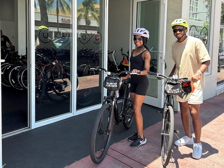 Two people standing next to bicycles in front of a store with a sign that reads 'UNLIMITED BIKING'. 5