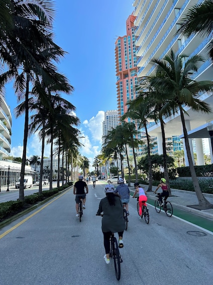 A street lined with palm trees and modern buildings, with cyclists on the road. 3