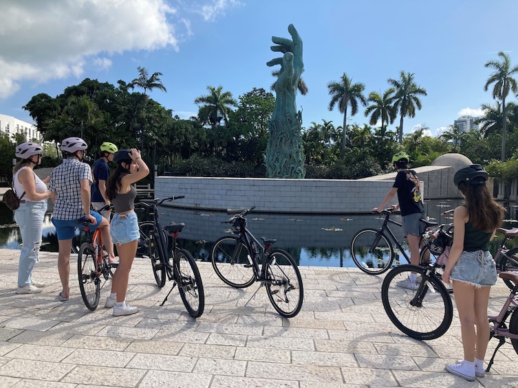 A group of people with bicycles near a water feature and palm trees in the background. 2