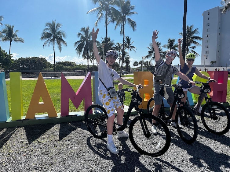 A group of people on bicycles with a colorful sign in the background. 1