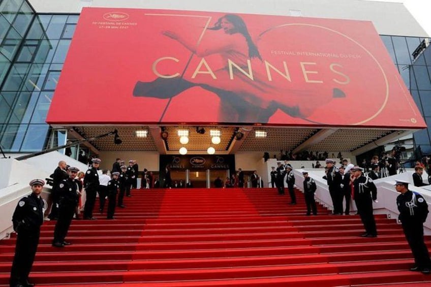 Ett evenemang med en röd matta, en stor skylt med texten ”Cannes”, röda trappsteg och personal i uniform. 2