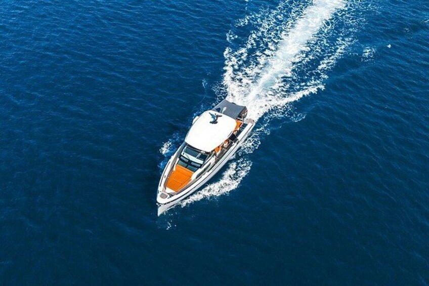 A white yacht with an orange deck moving through deep blue water, creating a wake behind it. 3