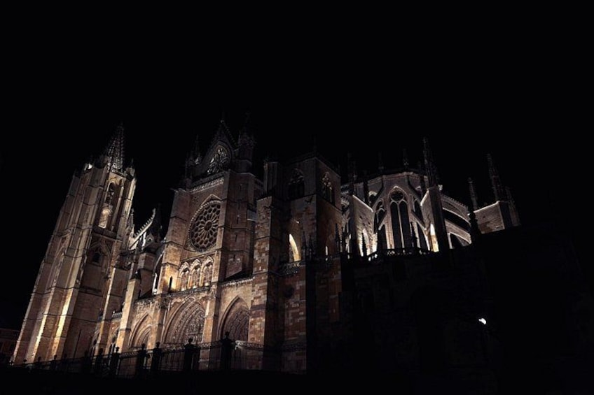 Eine große, beleuchtete Kathedrale in der Nacht mit aufwendiger gotischer Architektur, darunter Spitzbögen und filigraner Steinmetzarbeit. 1