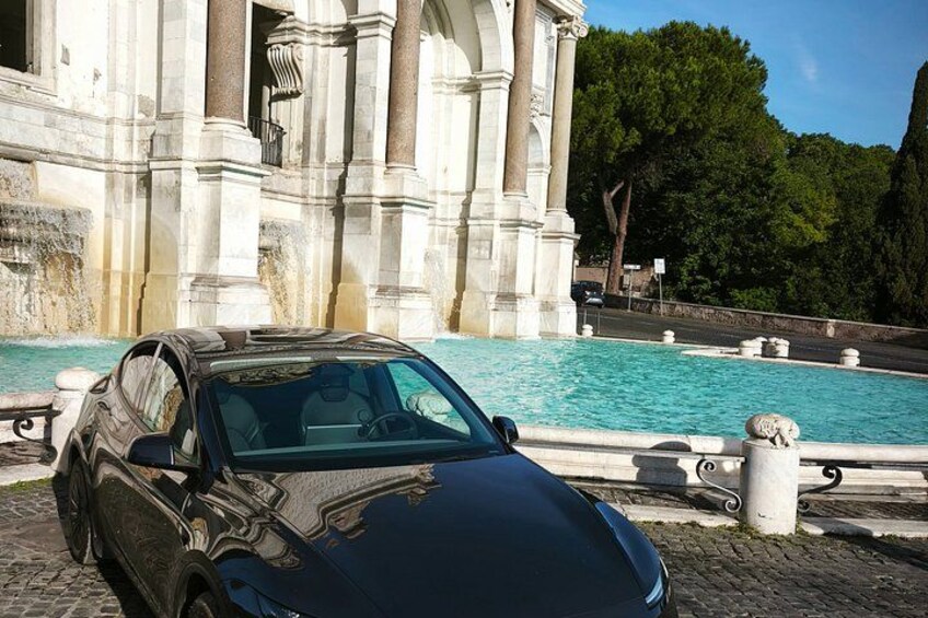 Un'auto decappottabile nera parcheggiata vicino a un edificio storico con una fontana. 3