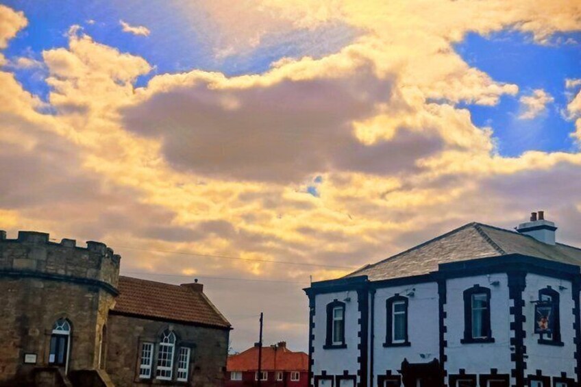 A historic building with a white facade and black trim, a stone tower, and a cloudy sky. 1