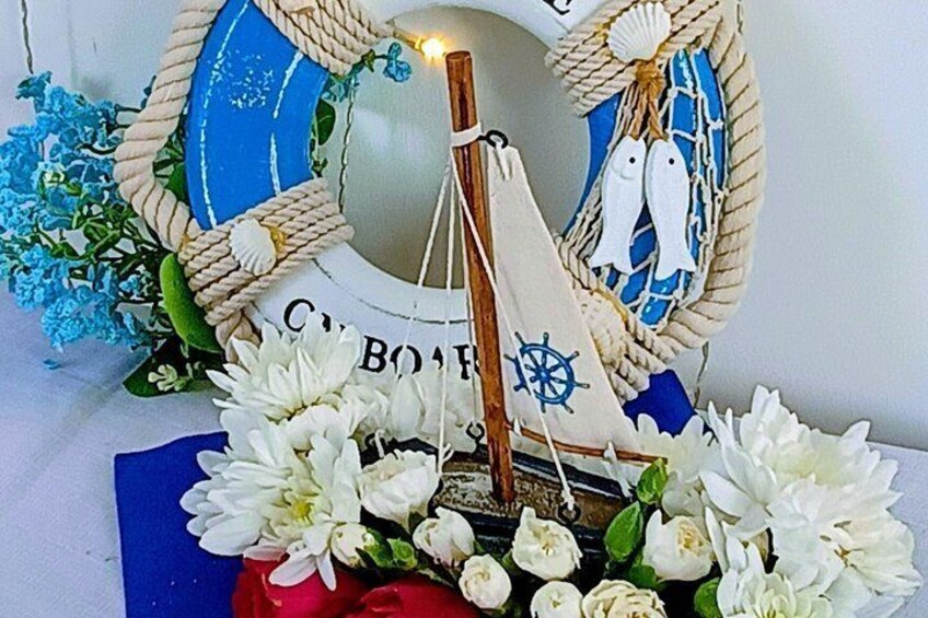 A decorative nautical-themed arrangement with a sailboat, white flowers, and a blue and white patterned backdrop. 3
