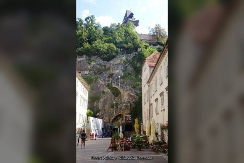 A street with buildings, a bridge, and a hill with a tower. 2